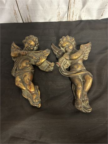 Two Statues Of Angels One Playing A Trumpet And One Playing The Violin