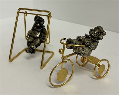 Two vintage clown figurines, one on a bike and one on a swing